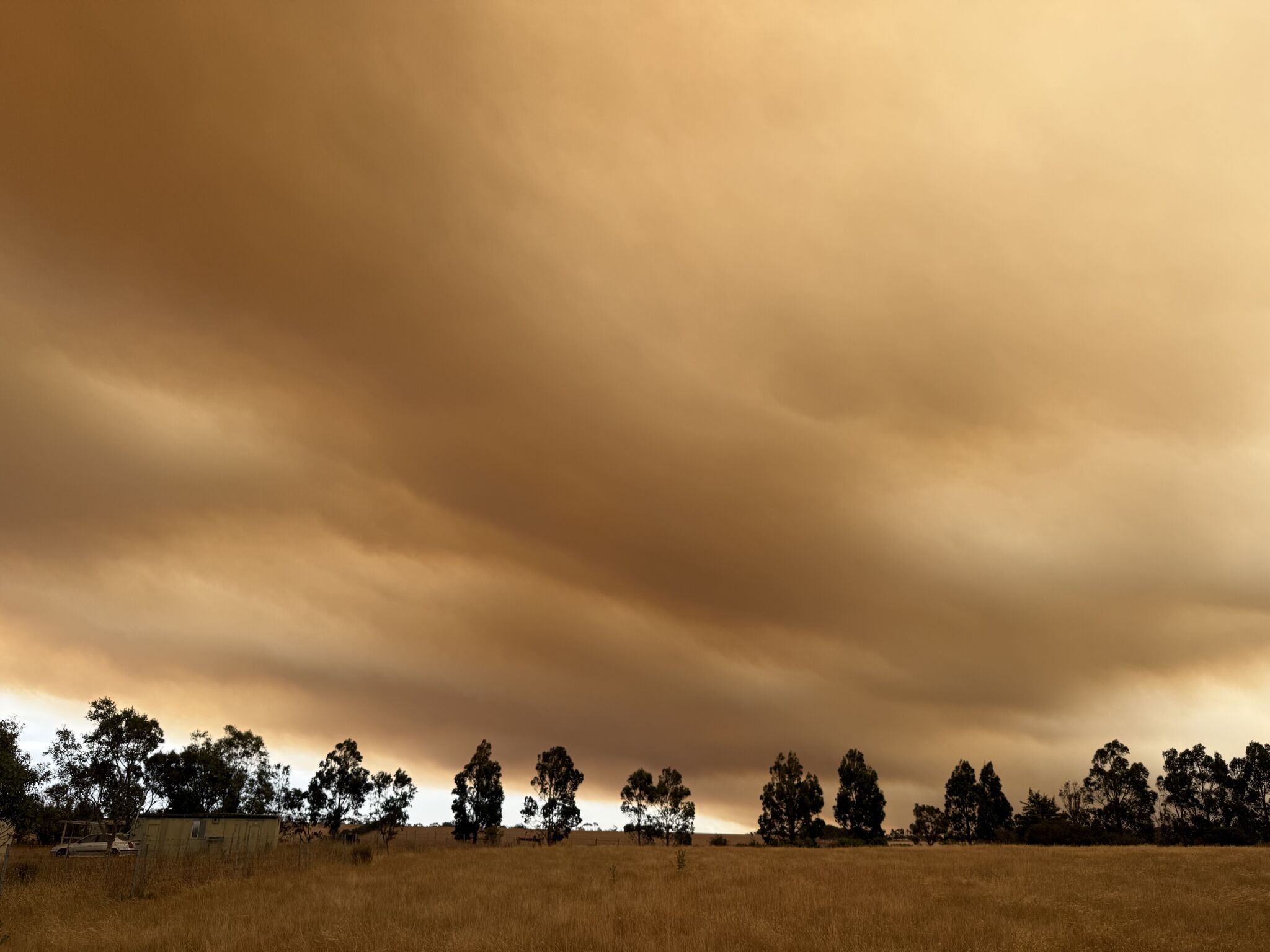 An open paddock with low clouds and orange sky, signalling a fire nearby